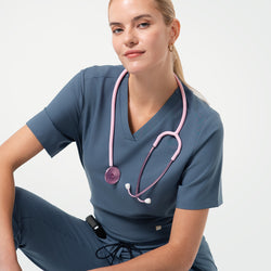 Image of Smiling medical professional poses in Smoky Blue scrub top and matching scrub pants, with a pink stethoscope draped around the neck.