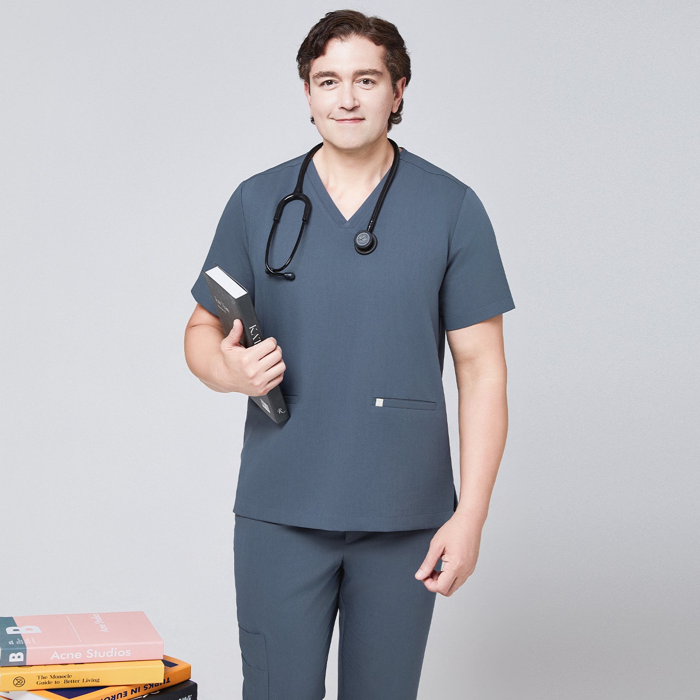 Image of Man in a smoky blue scrub set with a double-pocket V-neck top, holding a book and wearing a black stethoscope,Smoky Blue