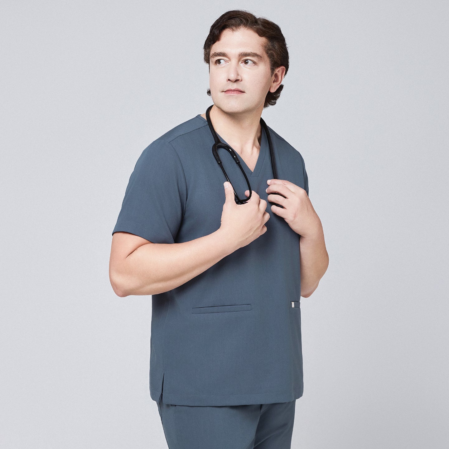 Image of Man wearing a smoky blue scrub set with a double-pocket V-neck top, holding a black stethoscope around his neck,Smoky Blue