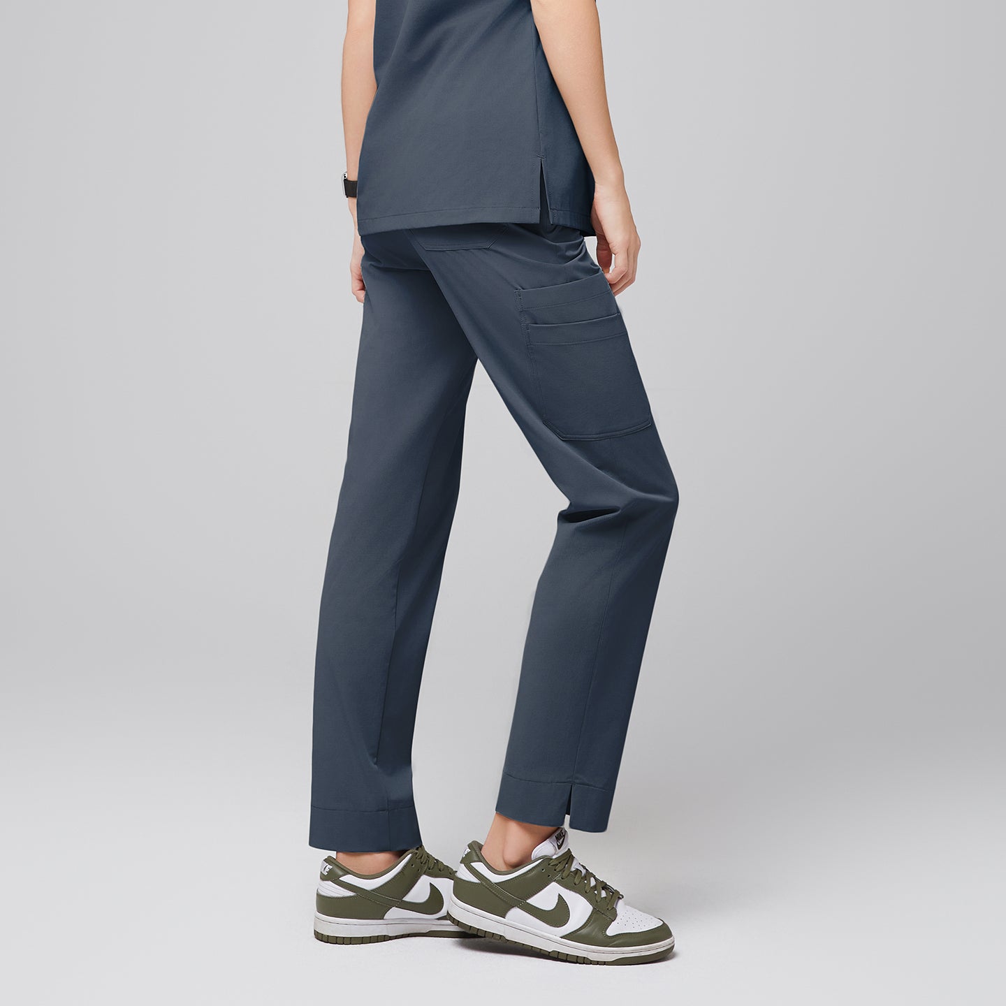 Image of Female wearing smoky blue scrub pants with side pockets, shown from the back, paired with green and white sneakers,Smoky Blue