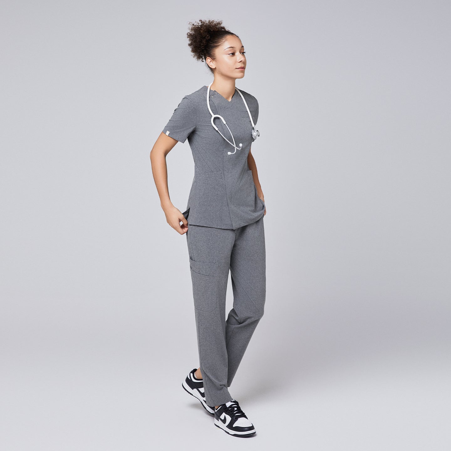 Image of Woman wearing Zenir soft gray front zipper scrub set with a stethoscope and black and white sneakers,Ash Gray