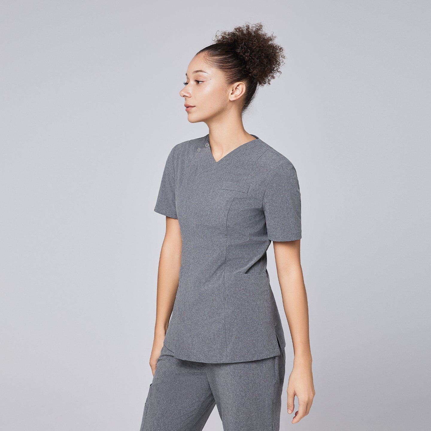 Image of Woman wearing Zenir soft gray front zipper scrub top with side profile, paired with matching pants,Ash Gray