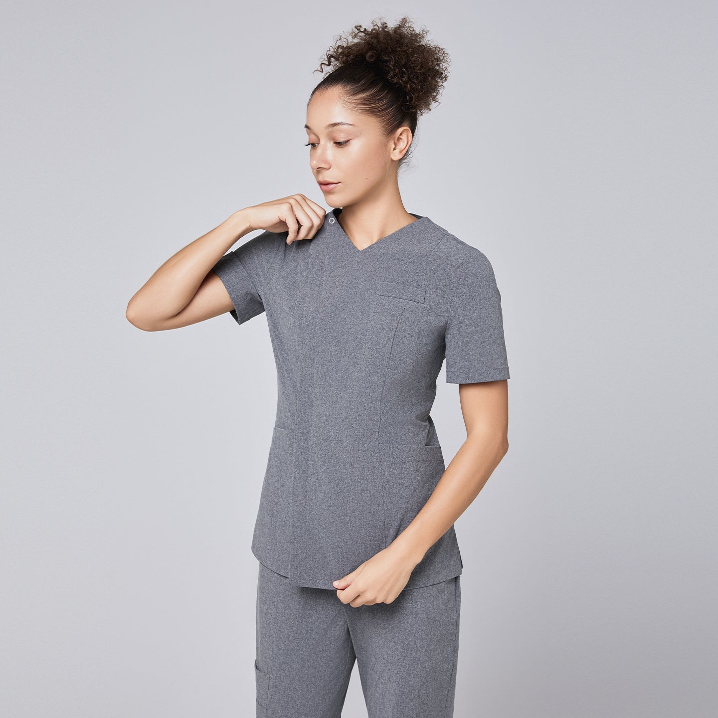 Image of Woman wearing Zenir soft gray front zipper scrub top, adjusting the zipper, paired with matching pants,Ash Gray