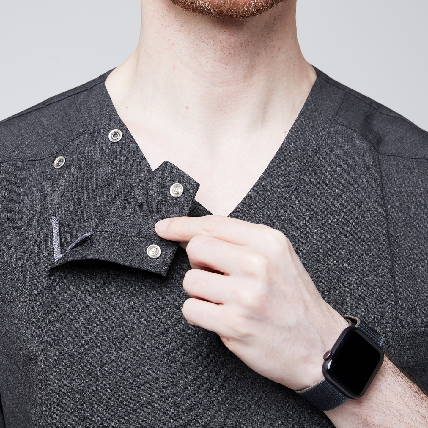 Close-up of a man demonstrating the functional snap buttons on the shoulder of a soft gray scrub top, highlighting its unique design detail,Charcoal Gray