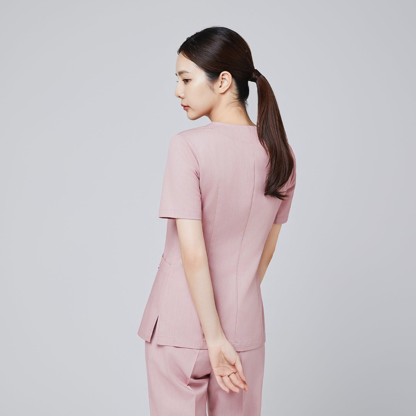 Back view of a female model wearing a soft pink scrub set, showcasing tailored stitching and a relaxed pose,Soft Pink