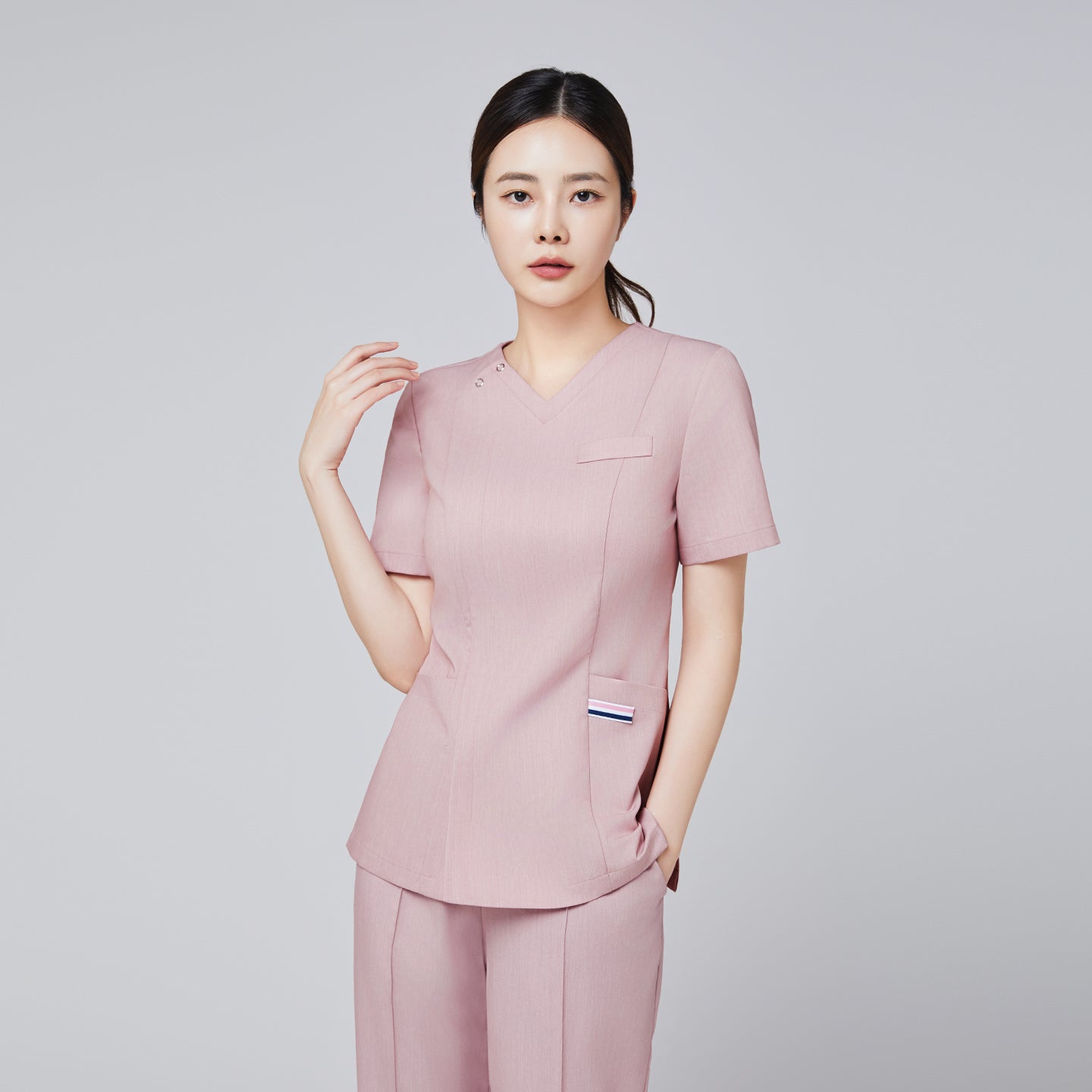 Image of Female model wearing a soft pink scrub top with subtle pocket details and matching pants, posing with a graceful expression,Soft Pink
