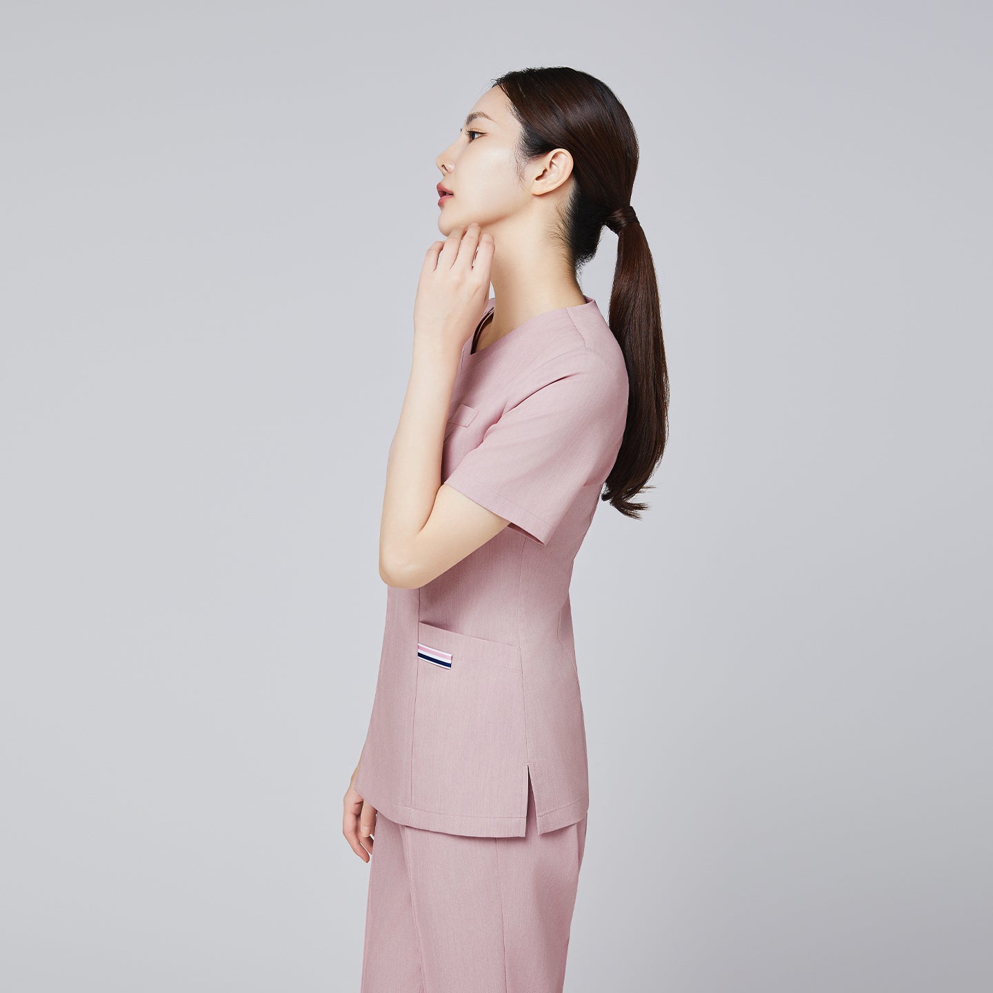 Image of Side profile of a female model wearing a soft pink scrub set with subtle pocket details, hair tied in a ponytail,Soft Pink