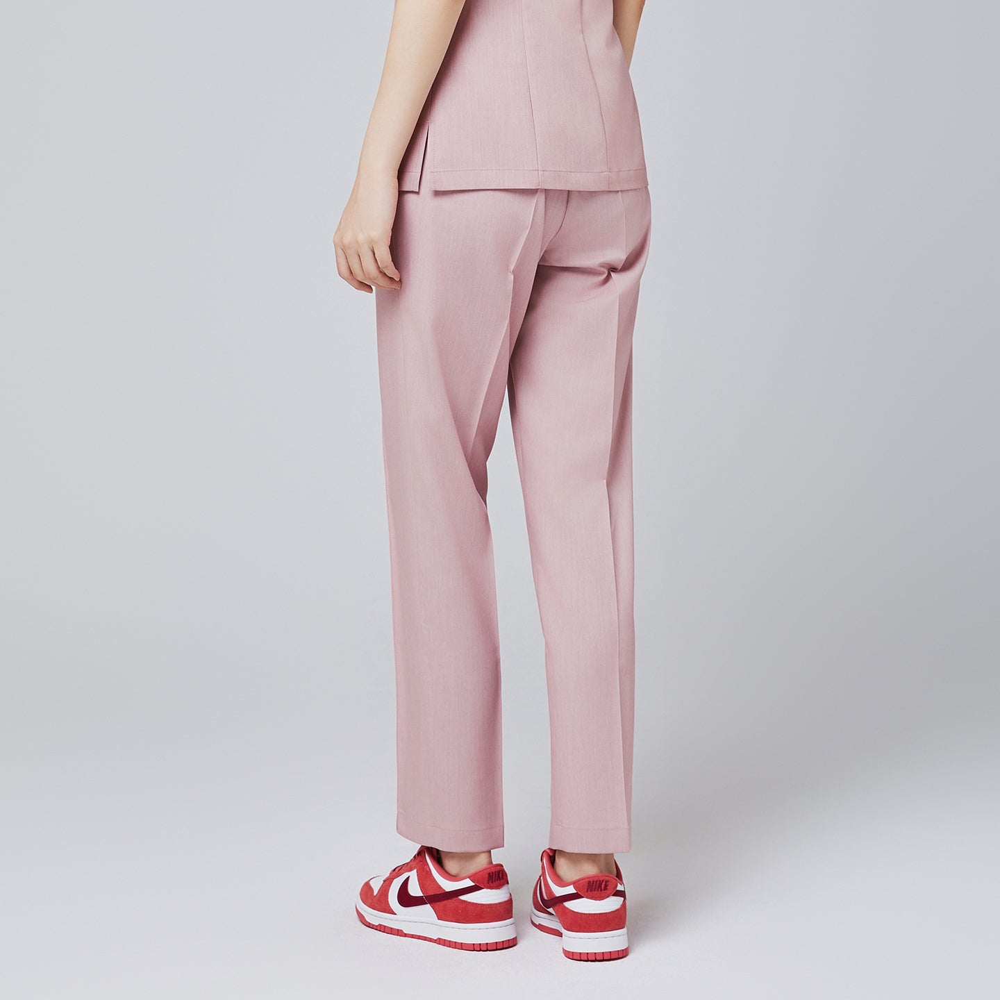 Image of Back of soft pink straight scrub pants with line banding detail, with matching soft pink scrub top and red sneakers,Soft pink