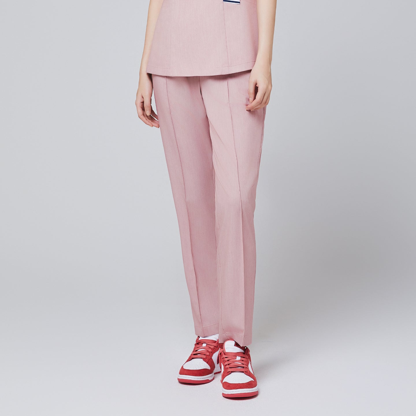 Image of Soft pink straight scrub pants with a line banding detail, with a matching soft pink scrub top and red sneakers,Soft pink