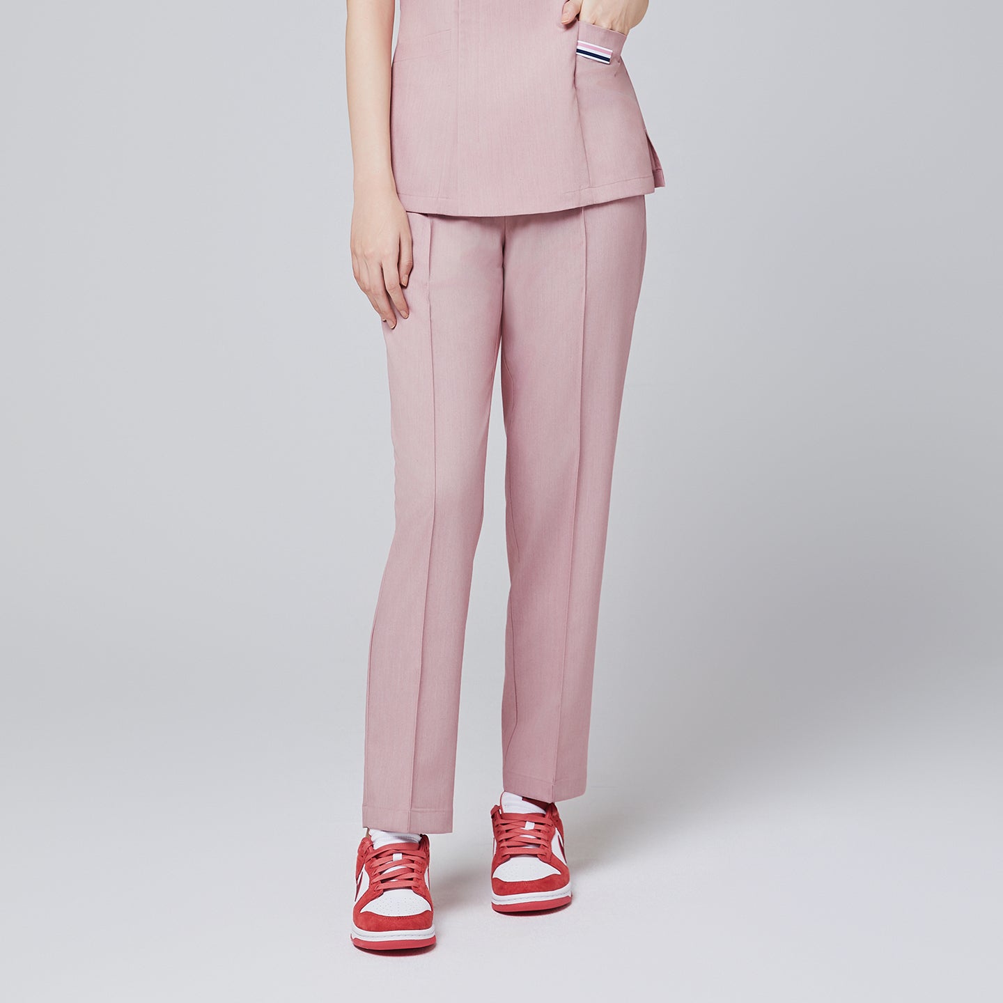 Image of Women with hand in soft pink scrub top pocket, wearing a soft pink straight scrub pants with red sneakers,Soft pink
