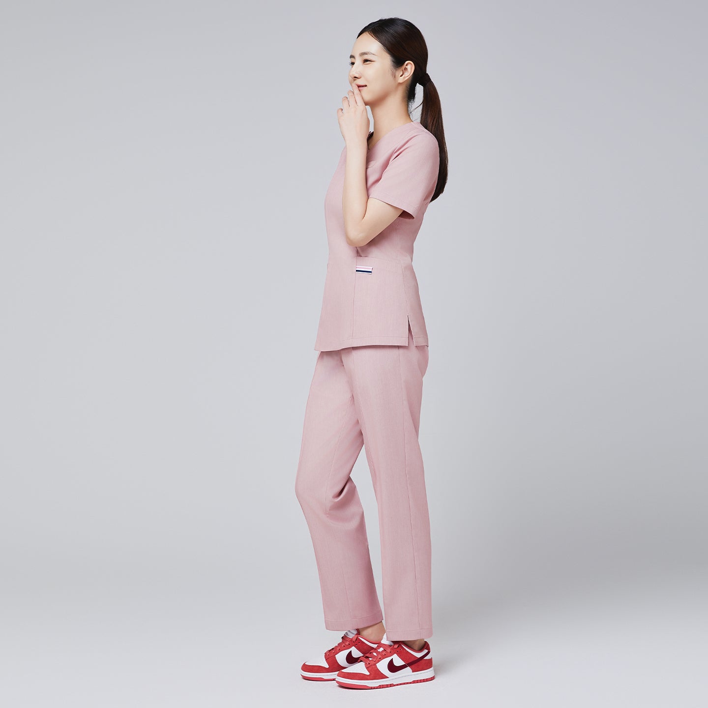Image of women with matching soft pink scrub top and straight soft pink scrub pants and red sneakers,Soft pink