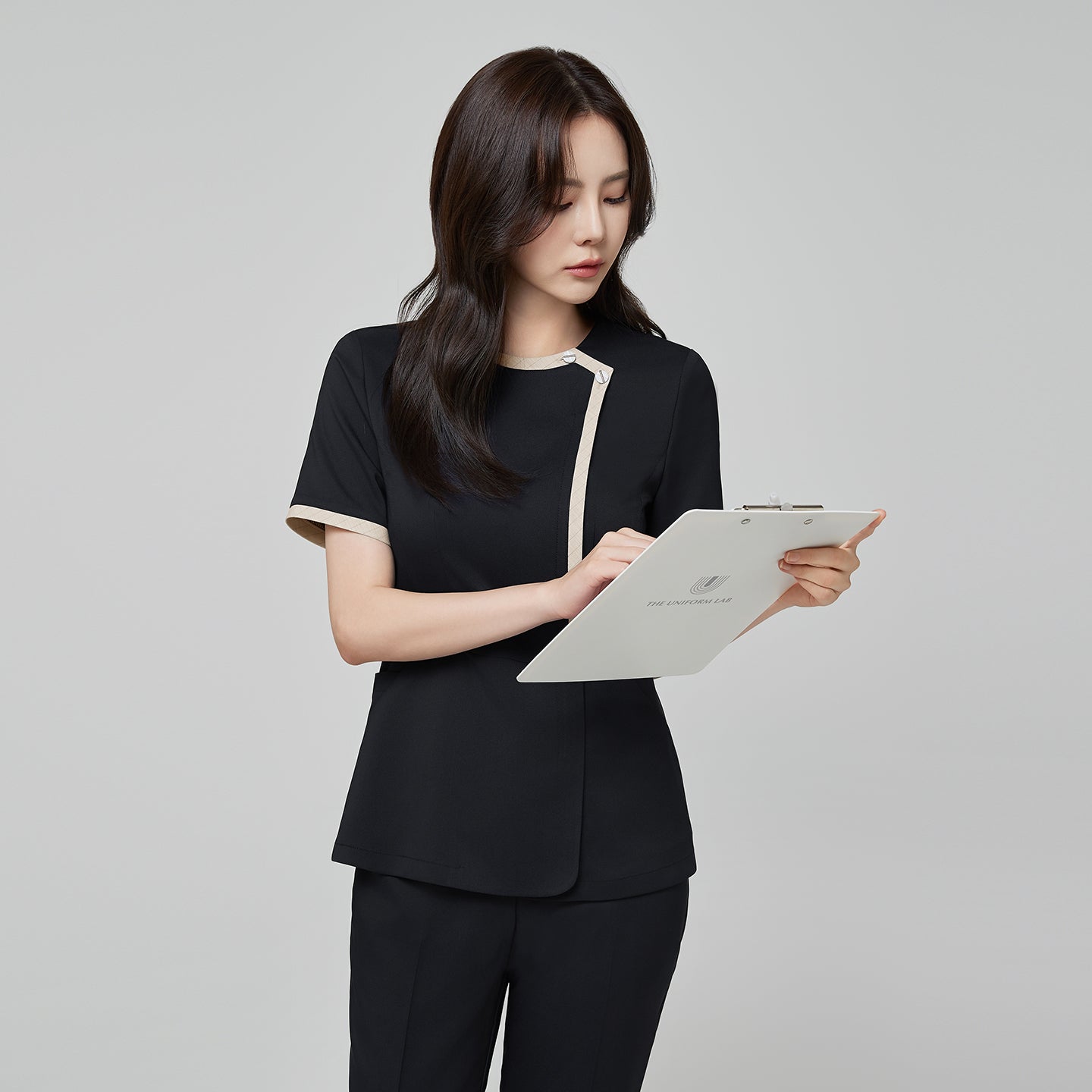 Image of Model wearing TUL NS-175 Women’s Check Beige Round Collar Scrub Top in Stretch Black, showing contrasting beige trim along the neckline and front.