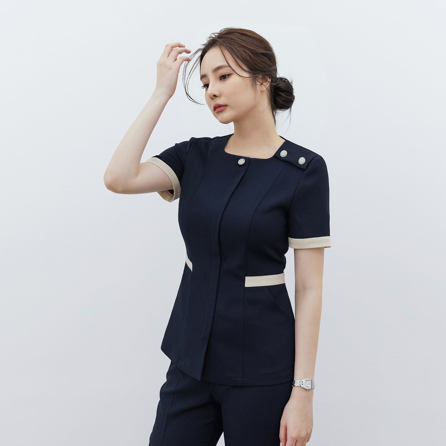 Model wearing TUL NCS-01 Women’s Classic Accent Scrub Top in Stretch Navy, showing contrast cuffs and waist detailing with dual accent buttons at the shoulder.