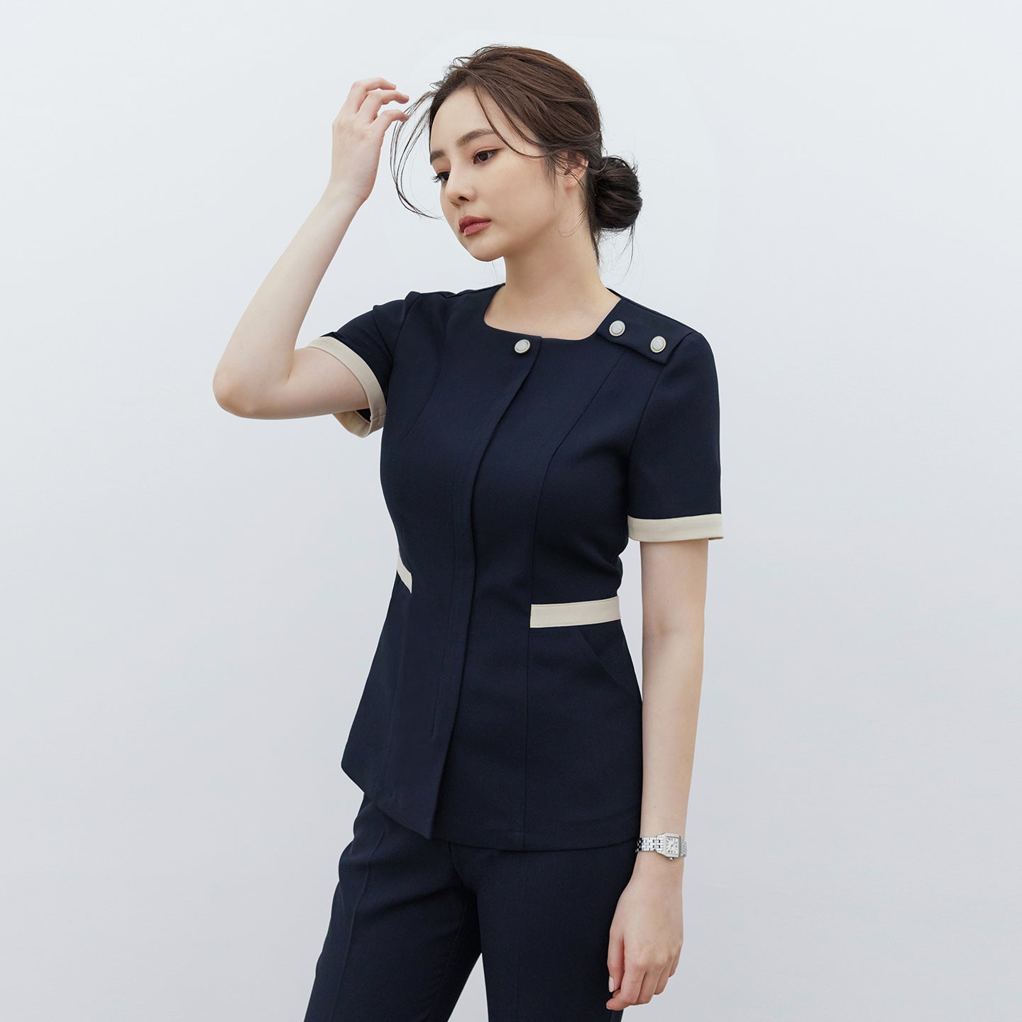Image of Model wearing TUL NCS-01 Women’s Classic Accent Scrub Top in Stretch Navy, showing contrast cuffs and waist detailing with dual accent buttons at the shoulder.