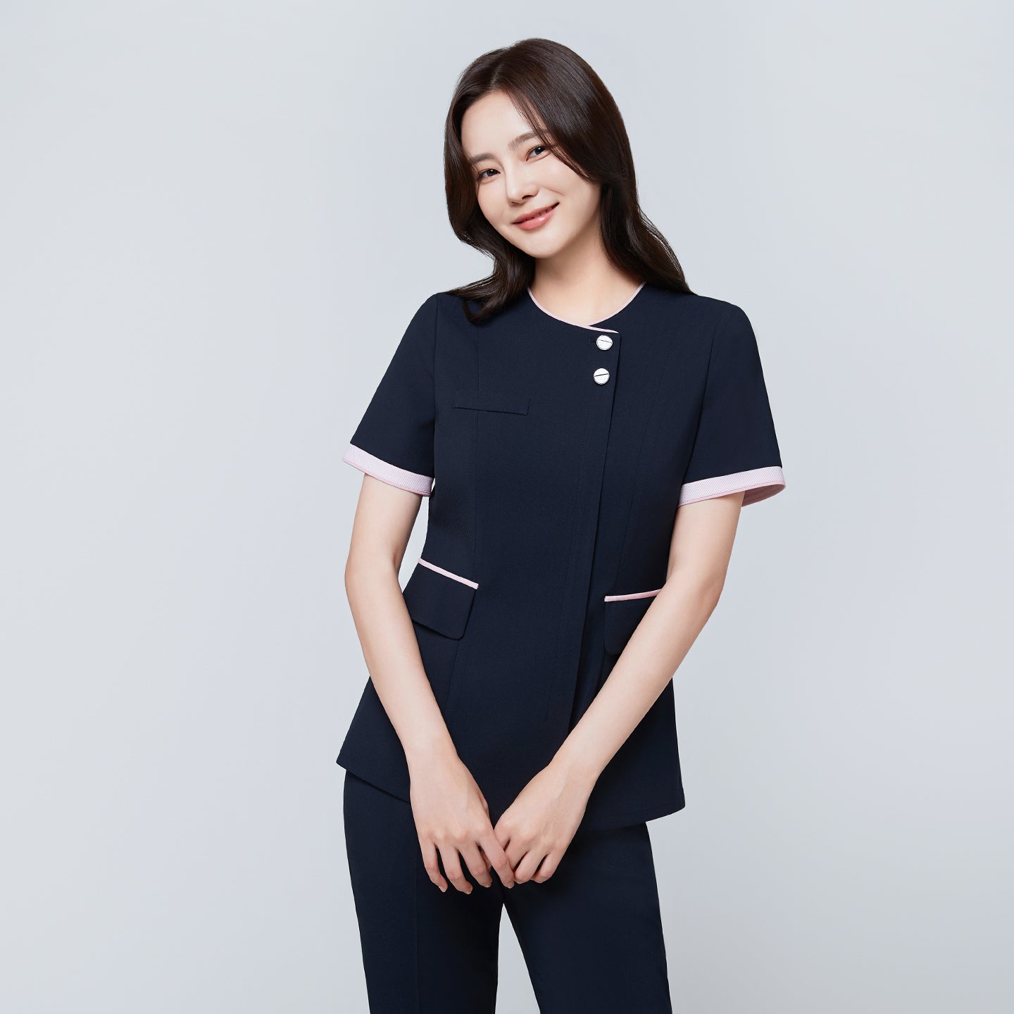 Model wearing TUL NCS-04 Women’s Blush Edge Scrub Top in Stretch Navy, smiling with arms crossed, emphasizing pink sleeve trim.