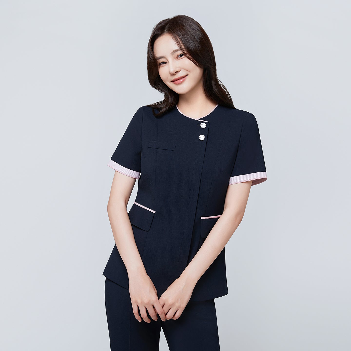 Image of Model wearing TUL NCS-04 Women’s Blush Edge Scrub Top in Stretch Navy, smiling with arms crossed, emphasizing pink sleeve trim.
