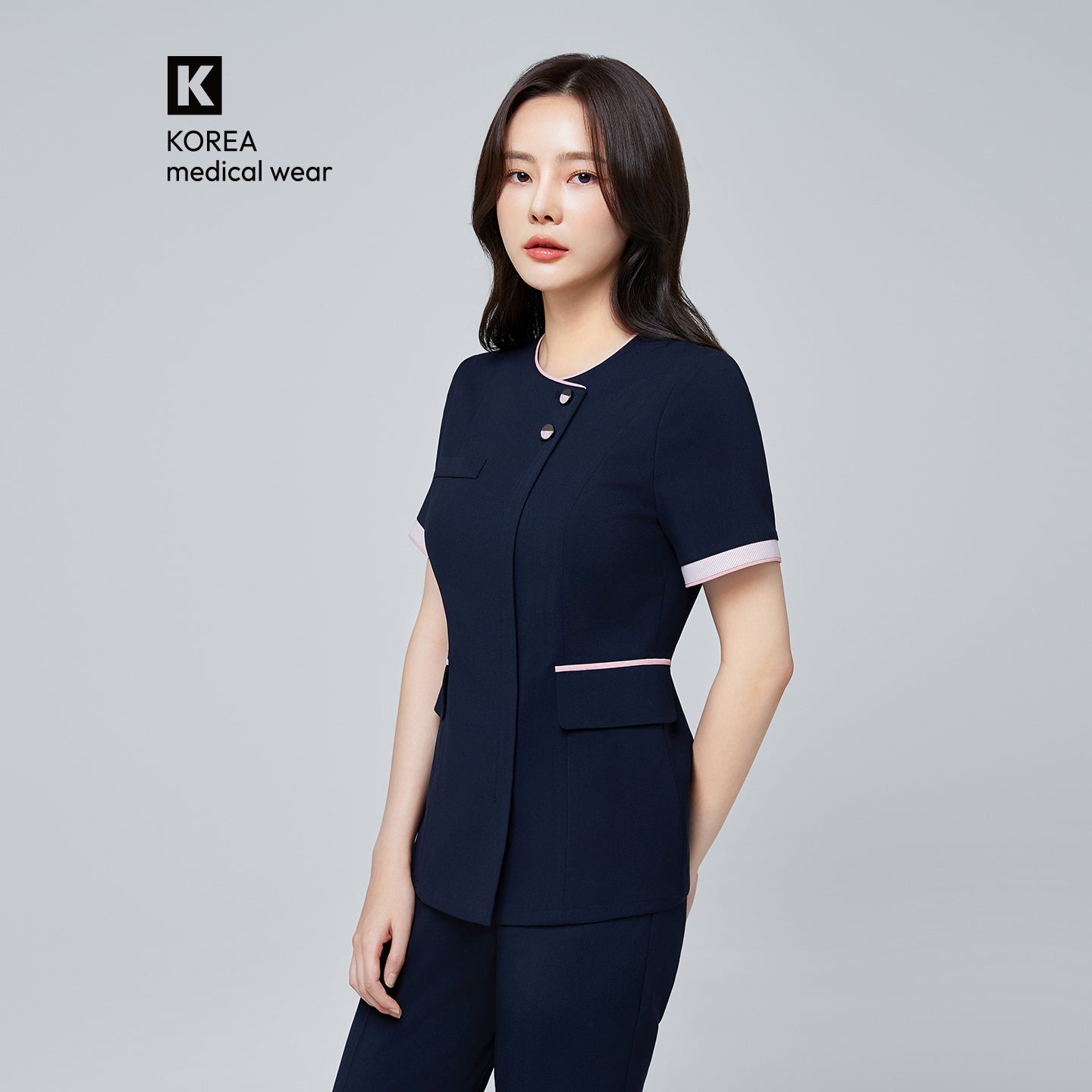 Image of Woman wearing a navy NCS-04 medical uniform with 'Korea Medical Wear' branding on a gray background.