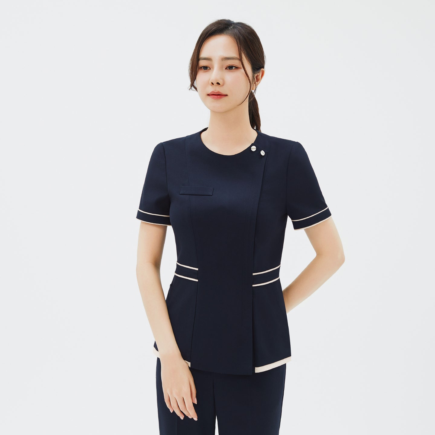 Image of Model wearing TUL NCS-07 Ivory Dual Tone Scrub Top in Stretch Navy, showcasing tailored seams and contrasting ivory piping for a modern style.
