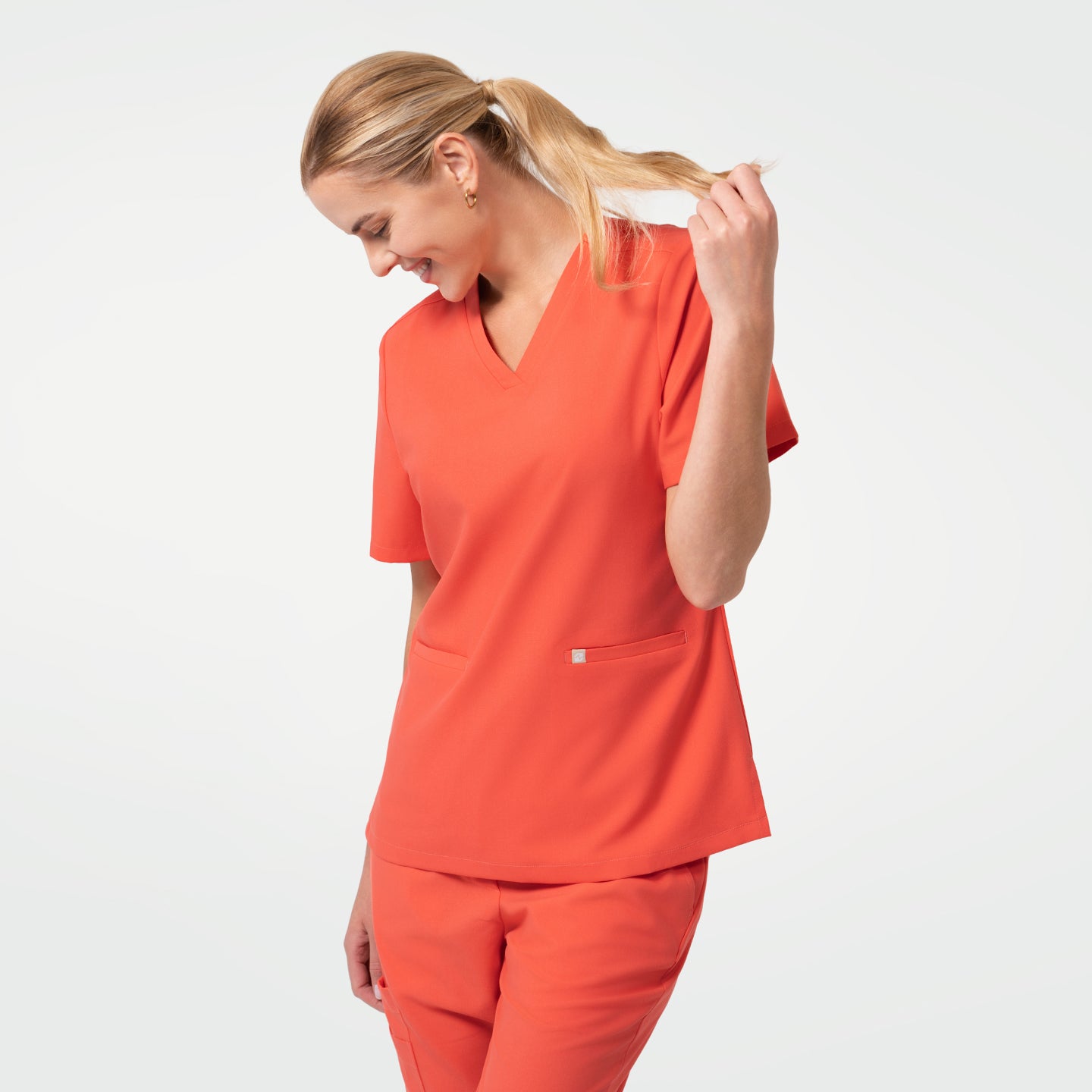 Image of The Tiger Orange Double Pocket Scrub Top highlights a flattering V-neck design with a cheerful orange tone.