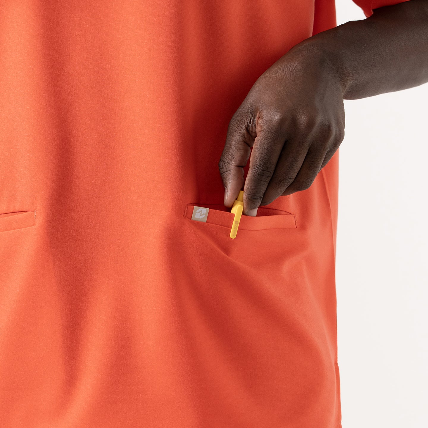 Image of The Tiger Orange Double Pocket Scrub Top features a vivid orange tone with practical double front pockets, ideal for holding everyday essentials.