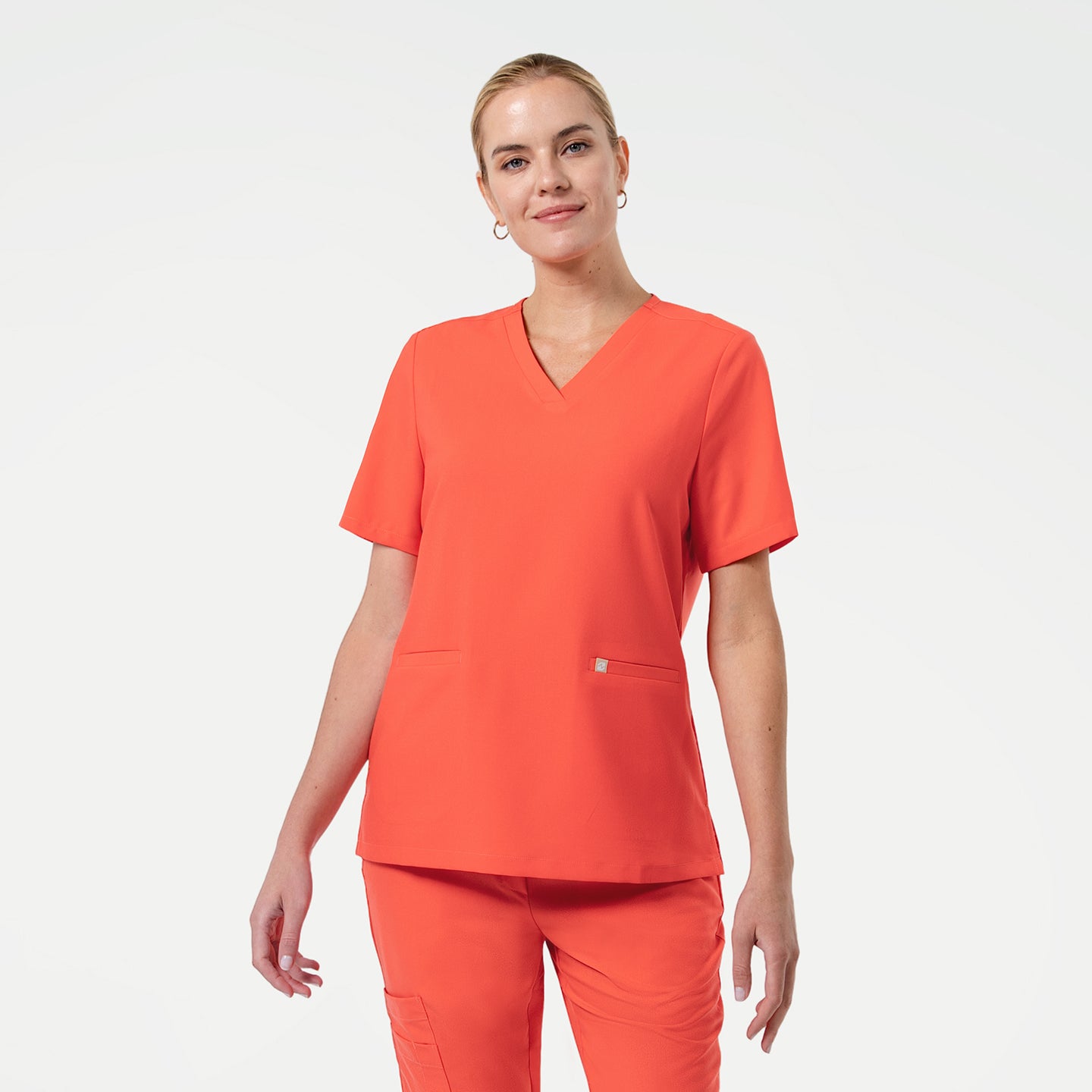 Image of Model dressed in the Women's Tiger Orange Double Pocket Scrub Top, facing forward with a slight smile, upper body shot