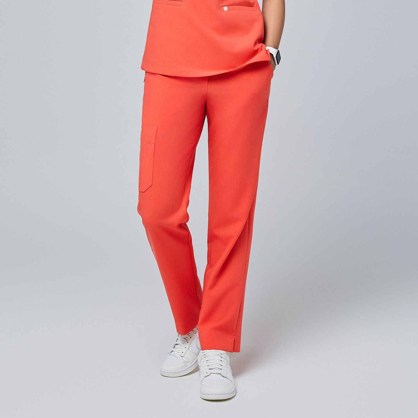 Image of Bright tiger orange straight-leg scrub pants with a split hem and side cargo pocket, paired with white sneakers on a neutral background,Tiger Orange