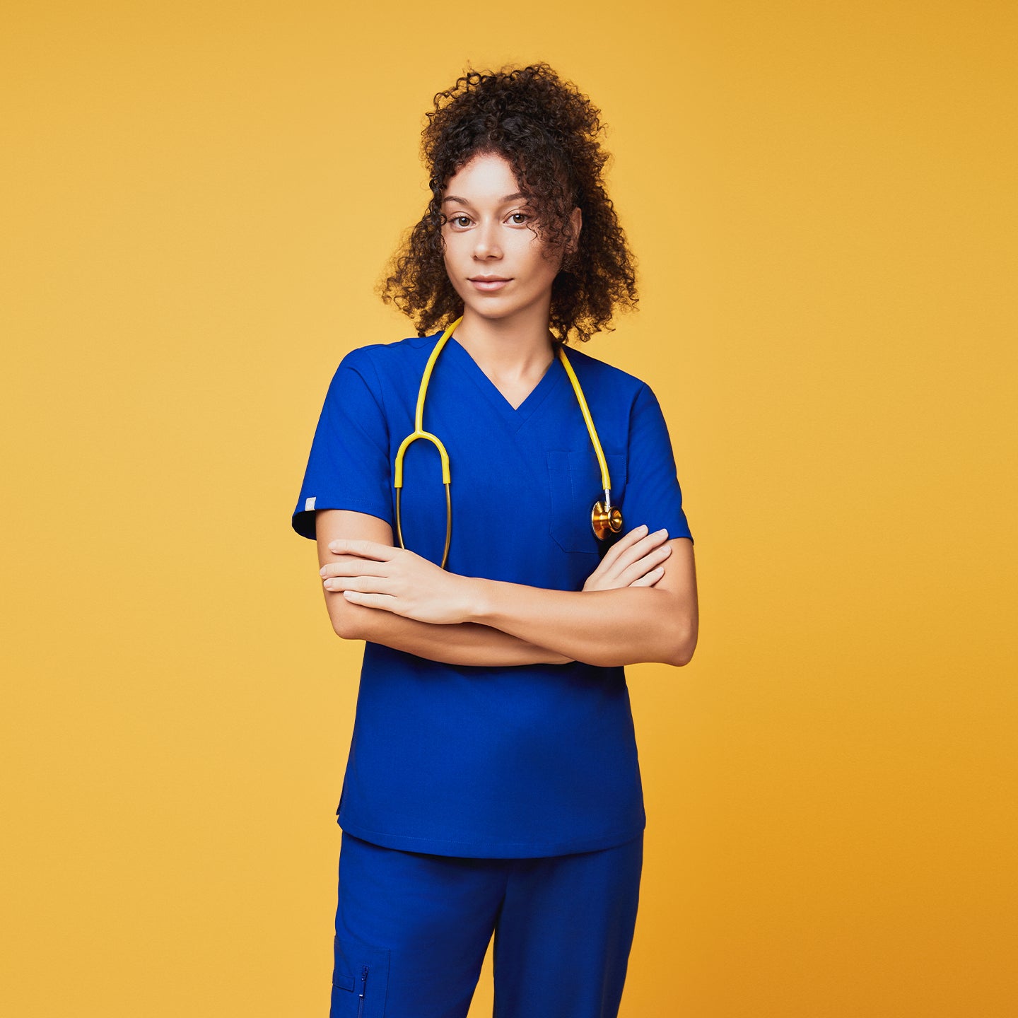 Image of Model wearing Zenir royal blue 3-pocket scrub top with a yellow stethoscope against a yellow background,Royal Blue