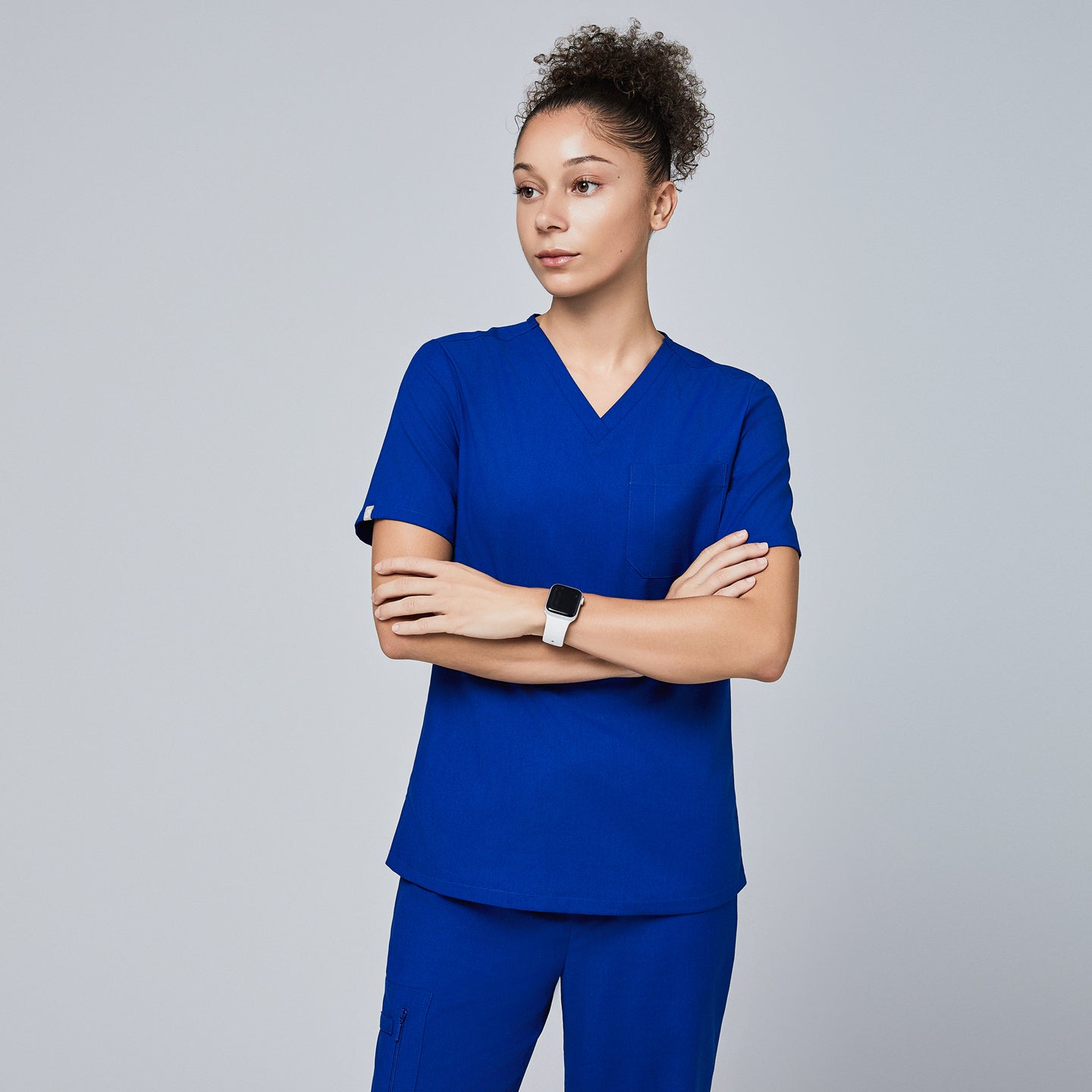 Model wearing Zenir royal blue 3-pocket scrub top with a yellow stethoscope against a yellow background,Royal Blue