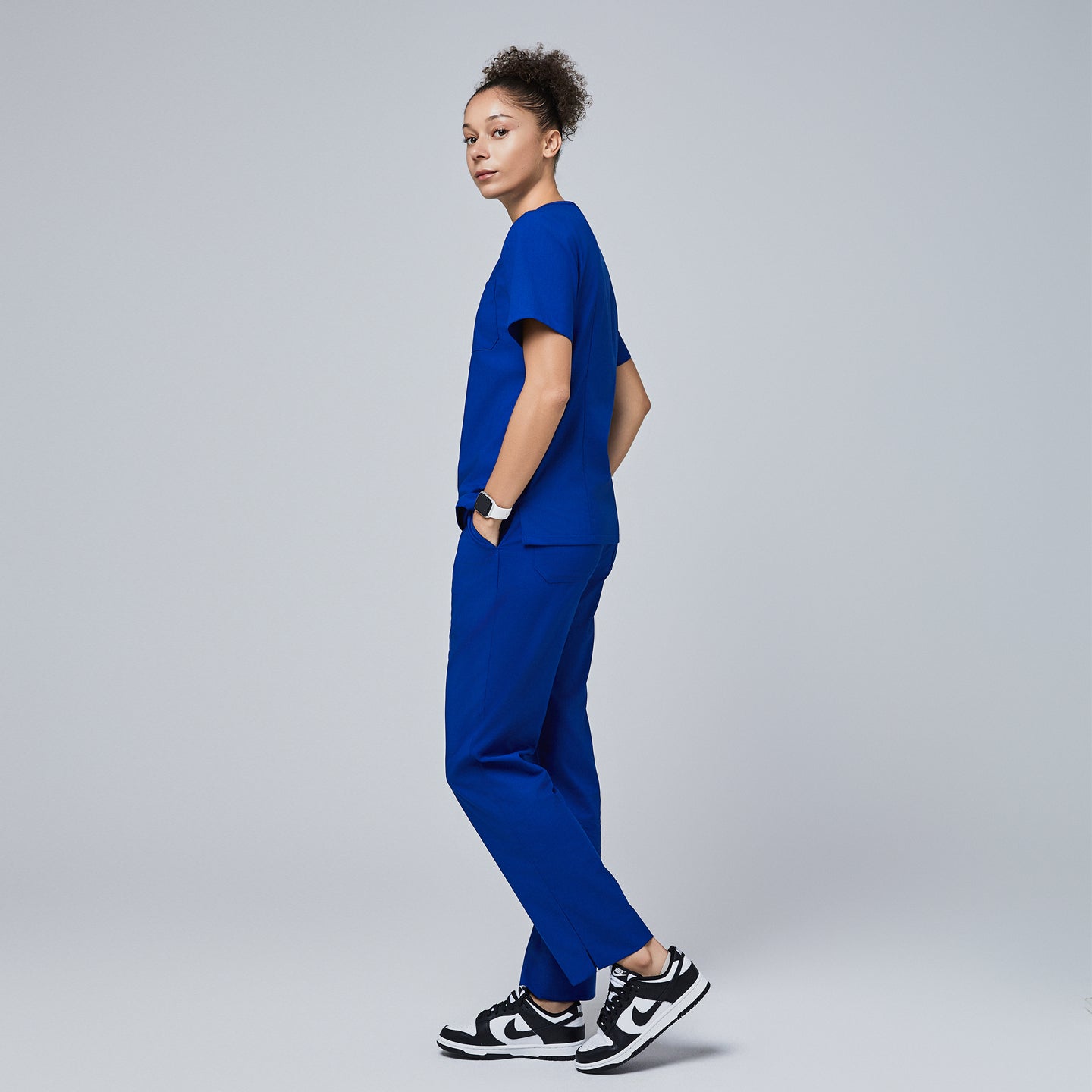 Model wearing Zenir royal blue scrub set with hands in pockets, viewed from the side, paired with black and white sneakers,Royal Blue