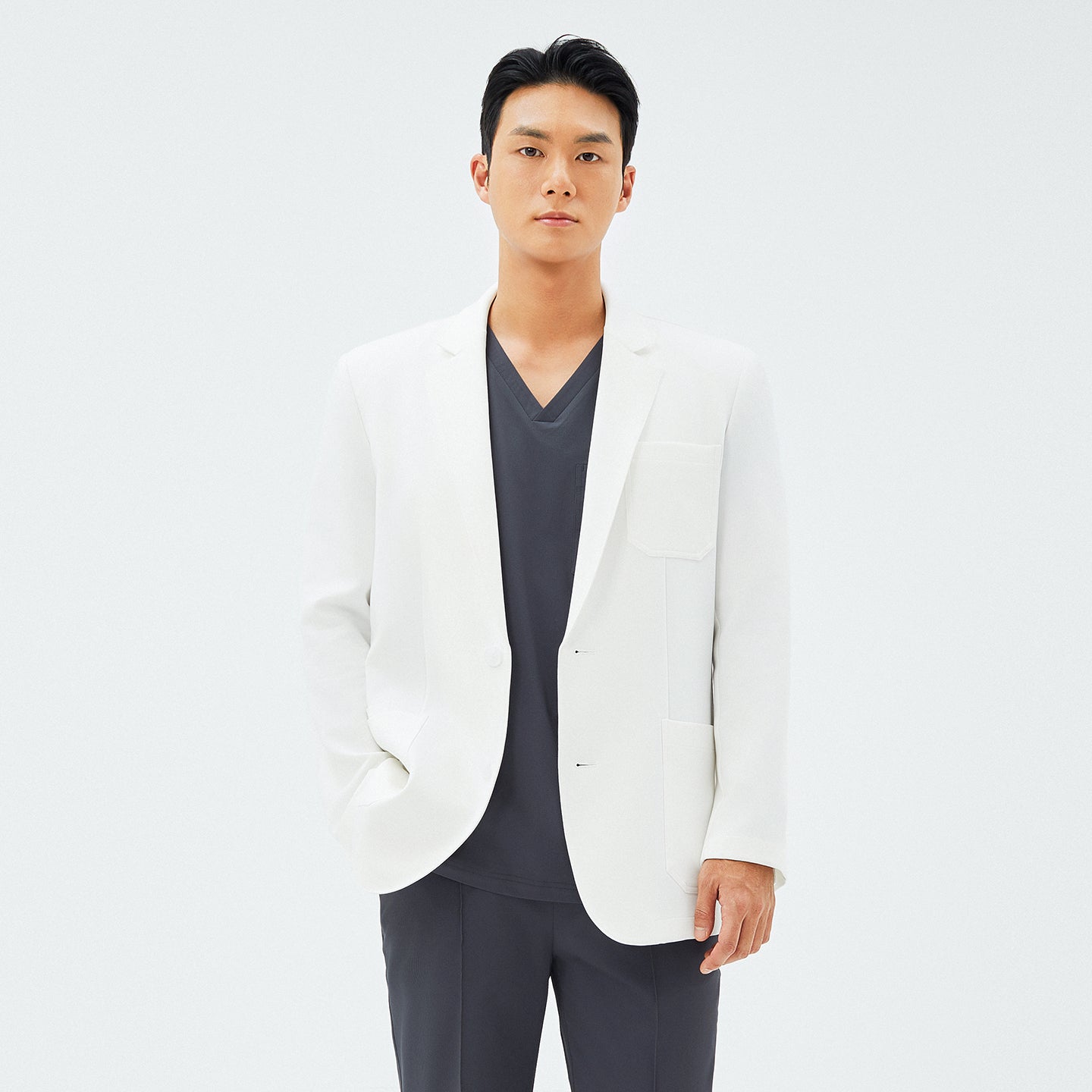 Image of Male model standing with one hand in his pocket, showcasing the TUL LCM-12 Men’s Short Lab Coat in White Ivory.