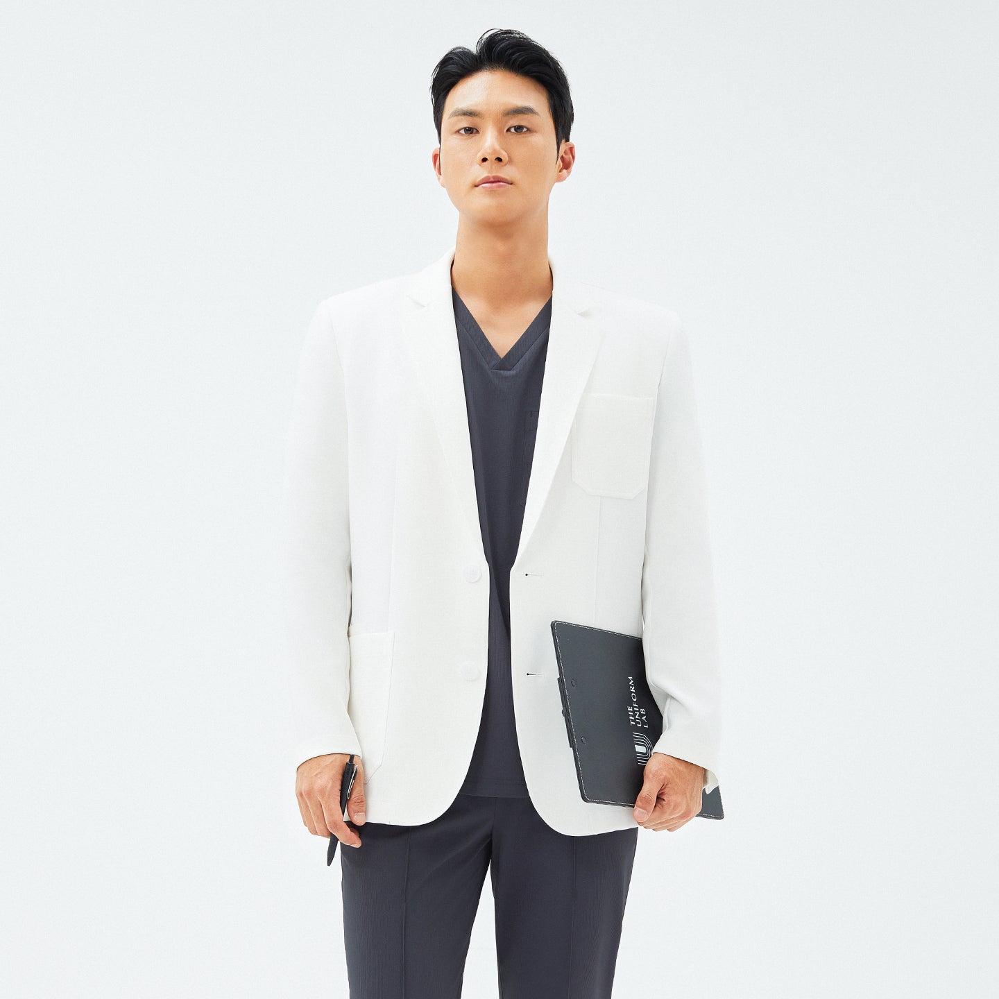 Male model holding a black folder and smartphone while wearing the TUL LCM-12 Men’s Short Lab Coat in White Ivory.