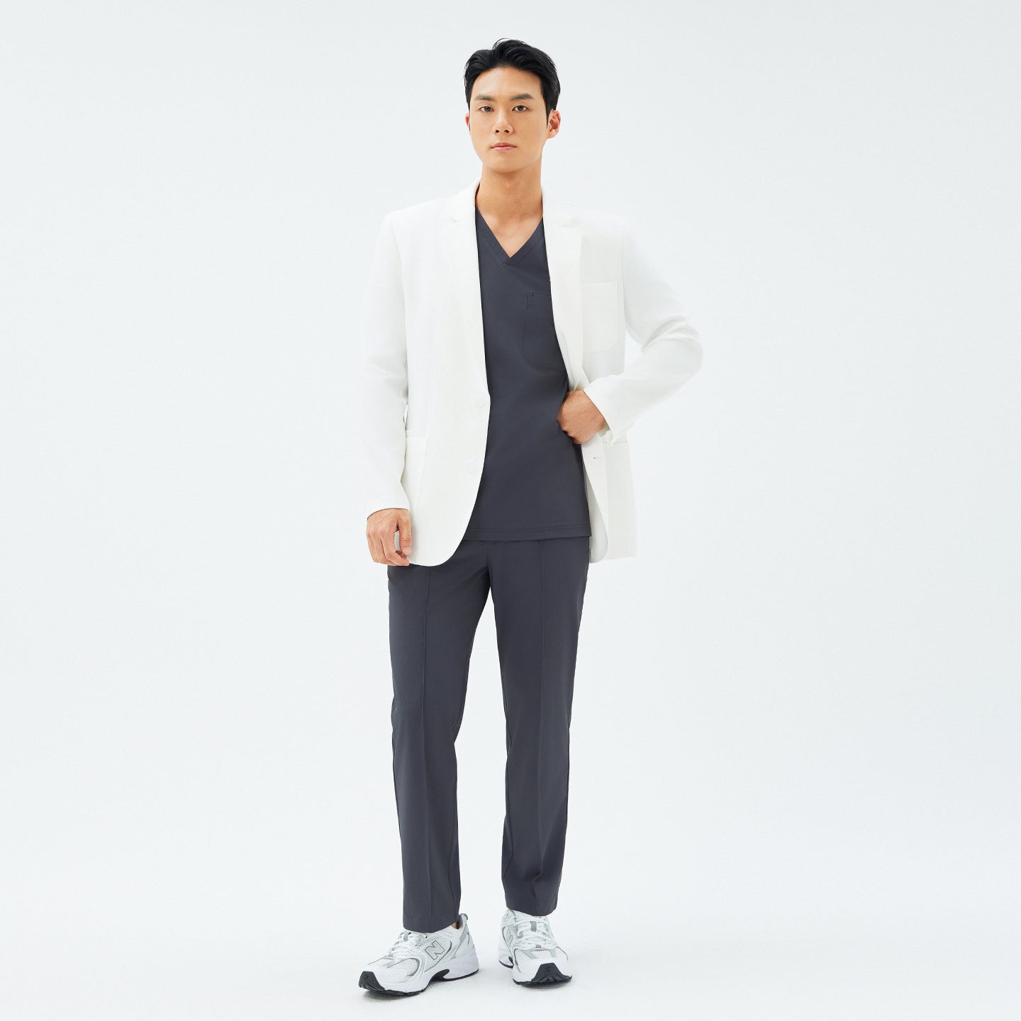 Full-body shot of a male model wearing the TUL LCM-12 Men’s Short Lab Coat in White Ivory over a dark V-neck scrub top and matching pants.