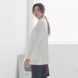 Image of Back angle of TUL LCW-01 Women’s Short Lab Coat in White Ivory, showing a slightly flared hem and vertical seams for a flattering fit. The model wears gray scrub pants and looks over her shoulder.