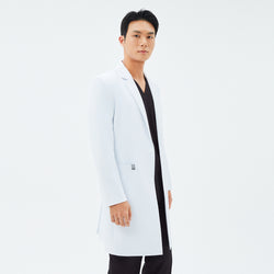 Image of Side angle of the TUL LCM-11 Men’s Long Lab Coat in White, showing a notched lapel, button closure, and fitted sleeves. The model wears black scrubs underneath.
