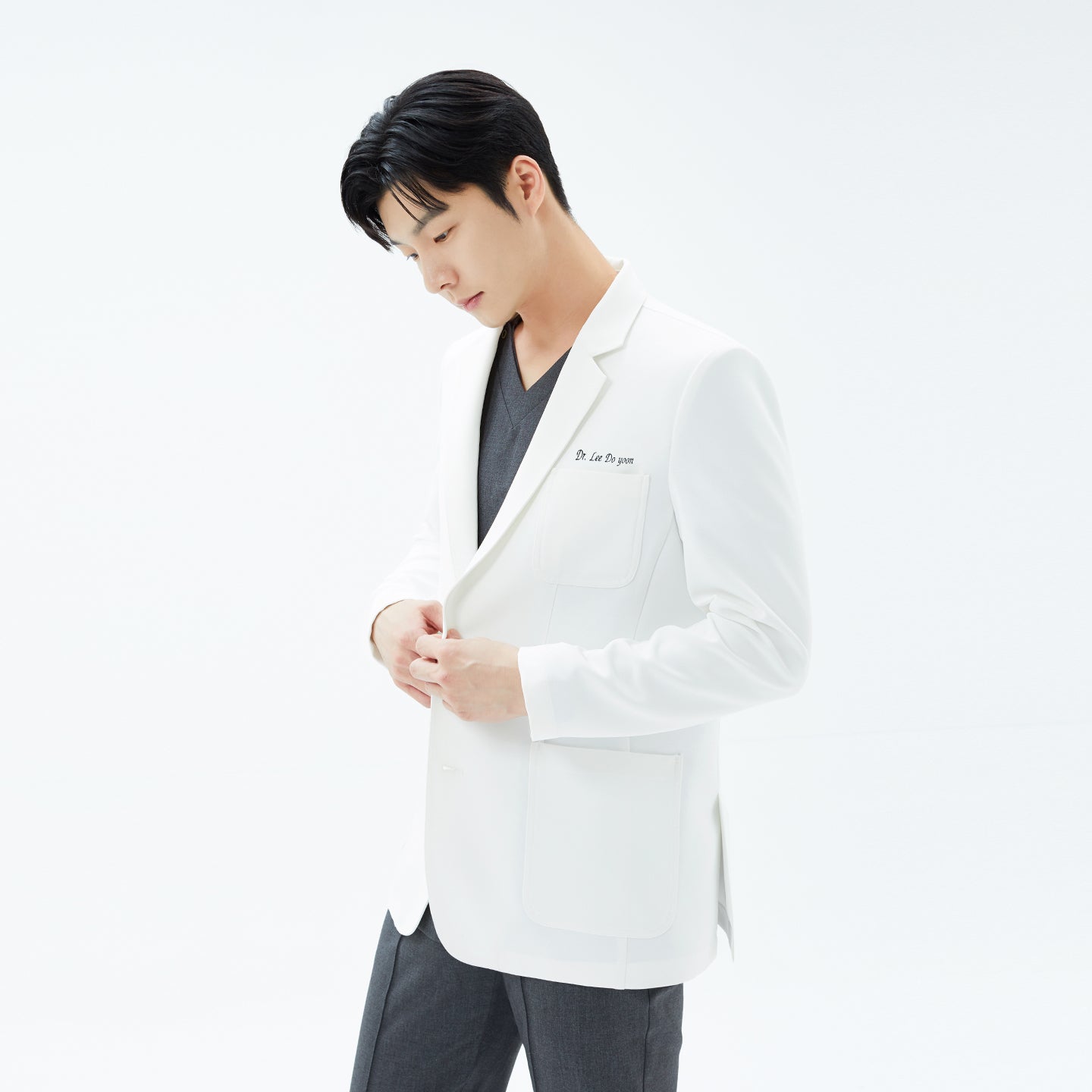 Image of Three-quarter front view of the model looking down while securing the coat’s buttons, emphasizing its hip-length cut.