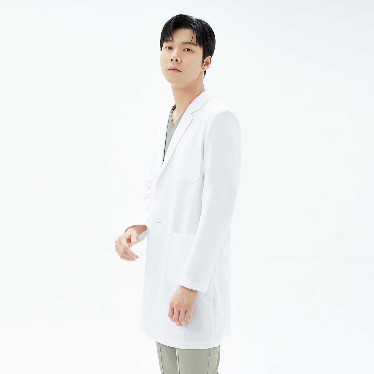 Image of Side-profile of the model facing left, showcasing the back seam and slit of the white TUL Men’s LCM-15 Core Long Lab Coat over khaki scrubs.