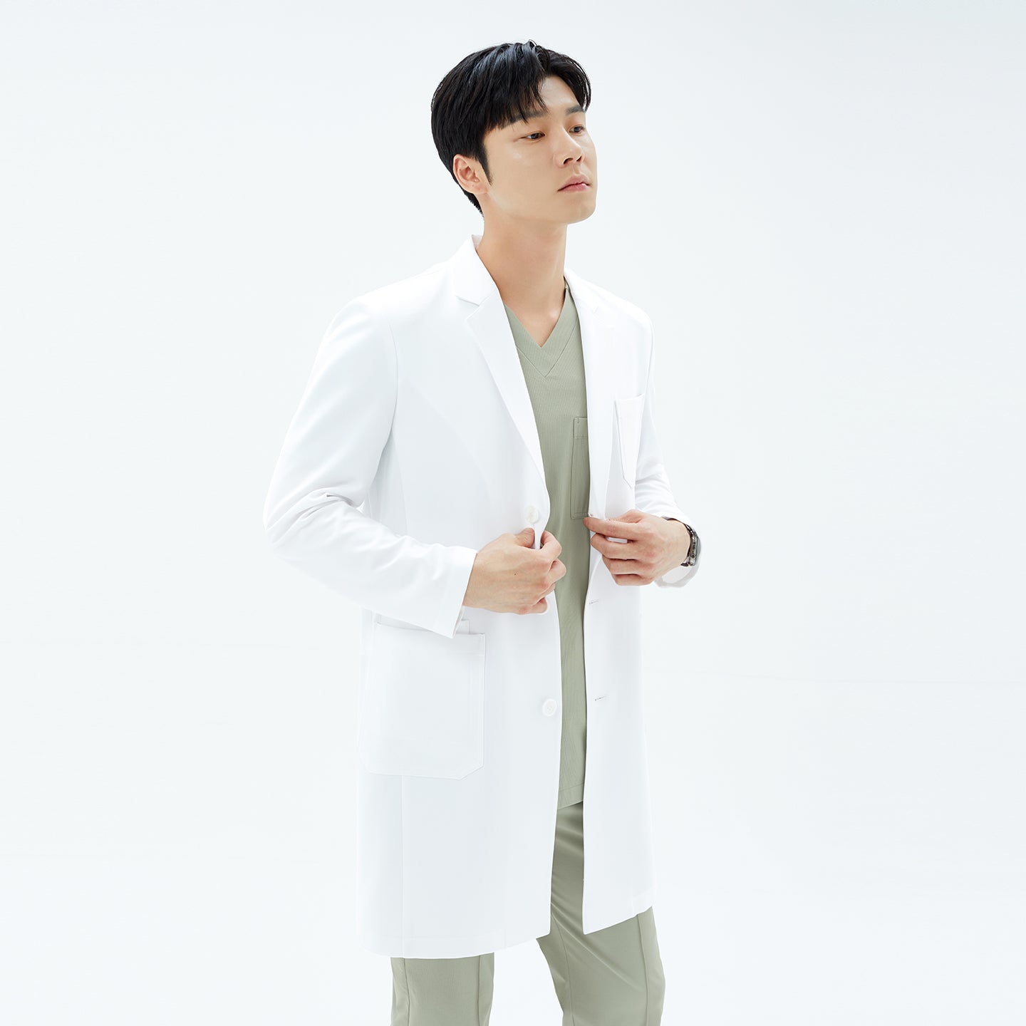 Image of Close-up three-quarter view of the model’s torso and face in the white TUL Men’s LCM-15 Core Long Lab Coat, coat pocket and tailored shoulder seam visible.