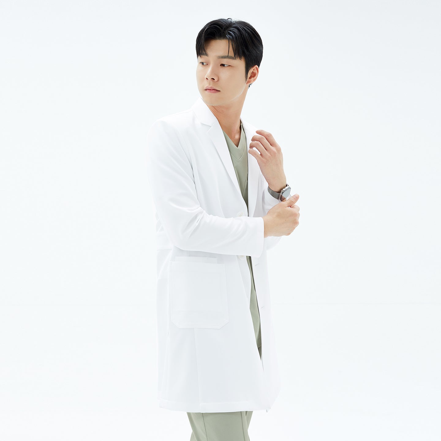 Image of Mid-length portrait of the model pulling down the sleeve of his white TUL Men’s LCM-15 Core Long Lab Coat, looking off to the side.