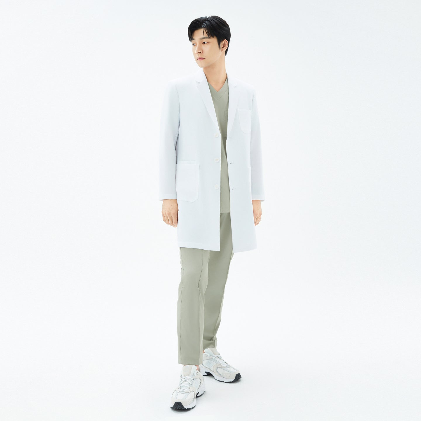 Image of Full-height image of the model standing straight in the white TUL Men’s LCM-15 Core Long Lab Coat and khaki scrubs, arms relaxed at his sides.