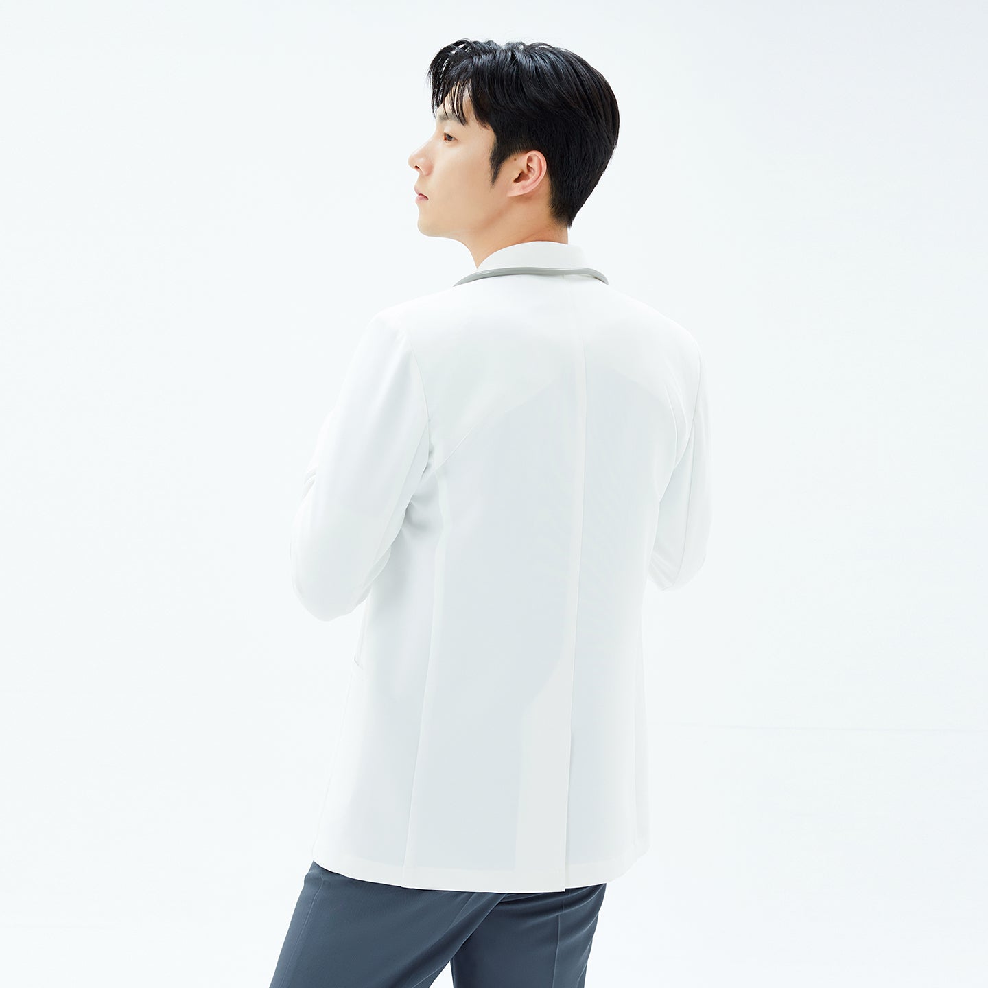 Image of Rear three-quarter view of the TUL Men’s LCM-17 UltraFit Short Lab Coat in White Ivory, showing its back vent and tailored fit as the model glances over his shoulder.
