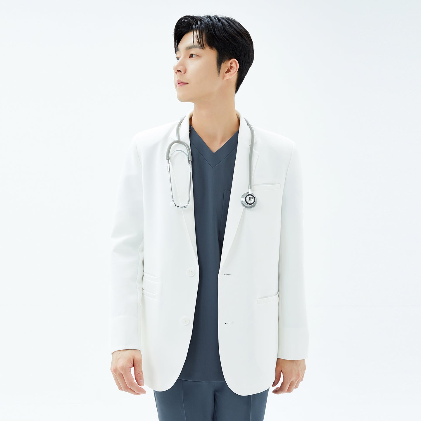 Image of Mid-torso shot of a model wearing the TUL Men’s LCM-17 UltraFit Short Lab Coat in White Ivory with a stethoscope over one shoulder, gazing to the left.