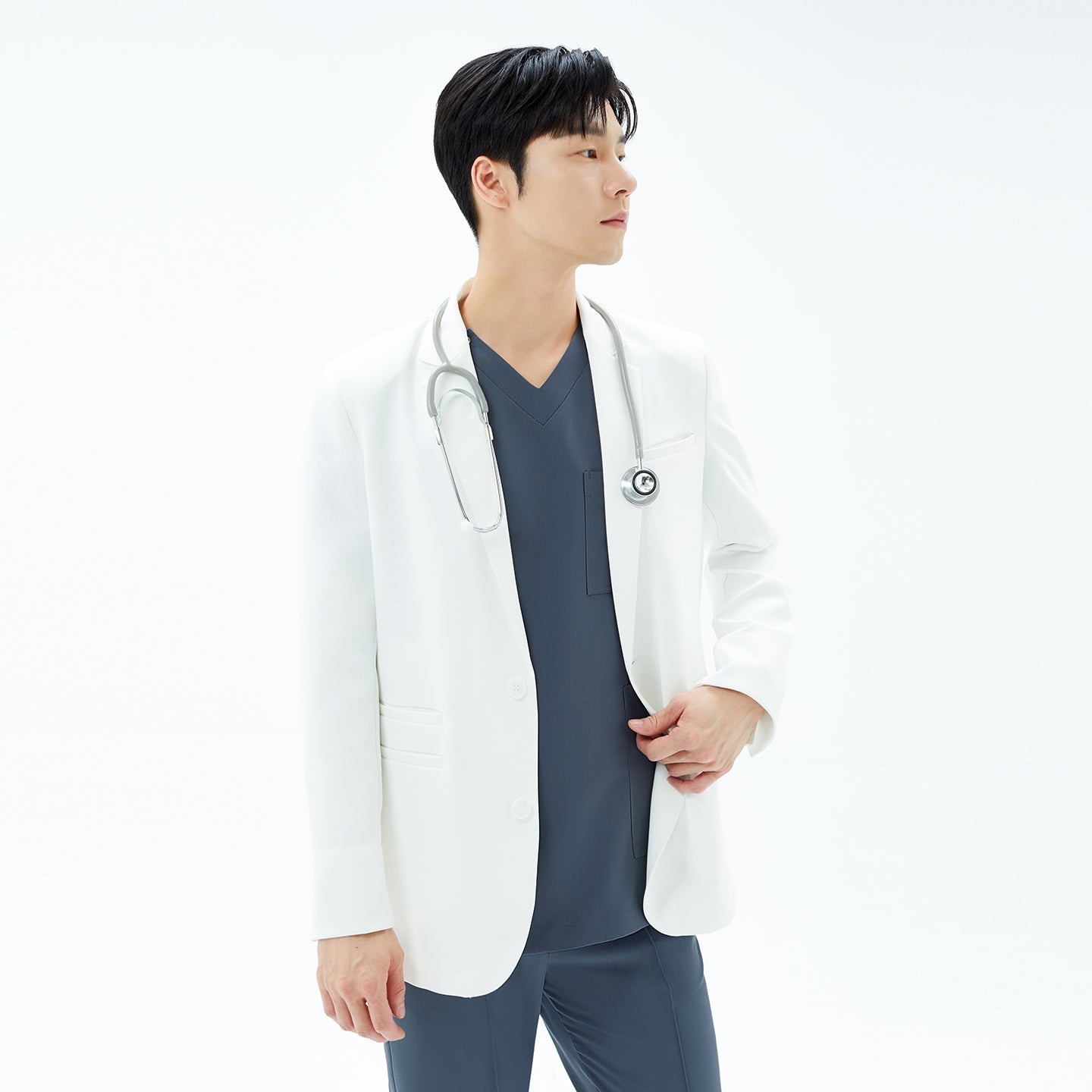 Image of Three-quarter view of a man in the TUL Men’s LCM-17 UltraFit Short Lab Coat in White Ivory, adjusting his cuff while holding a stethoscope and looking to the right.