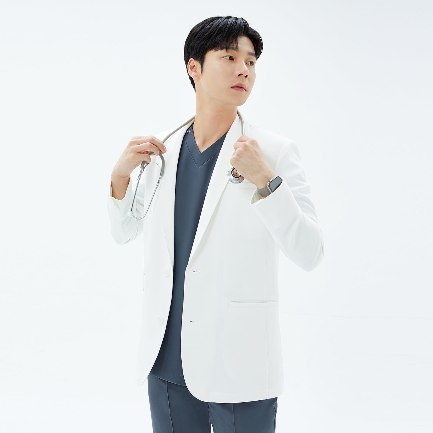 Image of Model draping a stethoscope around his shoulders while wearing the TUL Men’s LCM-17 UltraFit Short Lab Coat in White Ivory, looking off to the right.