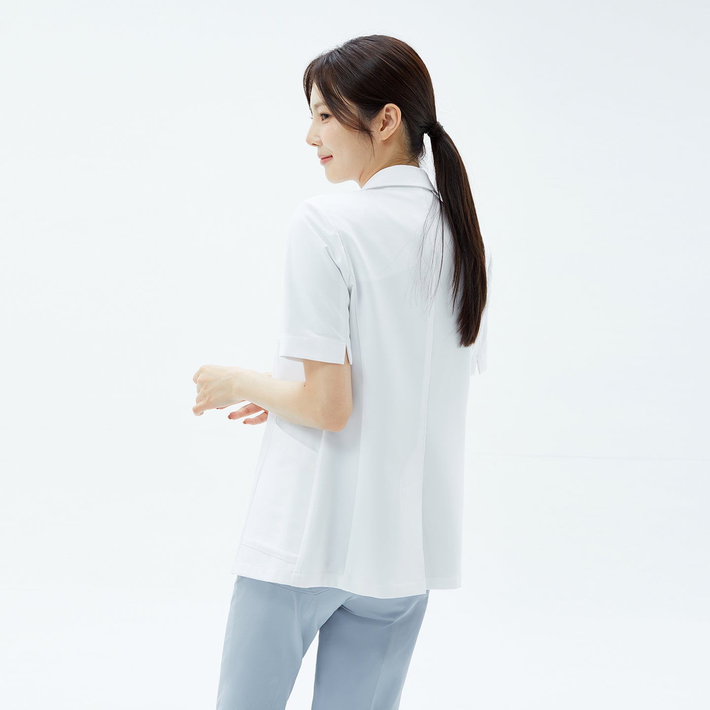 Image of Rear three-quarter view of the TUL Women’s LCW-15 Lightweight Short Sleeve Lab Coat – White showing its vented back seam and relaxed fit on the model.