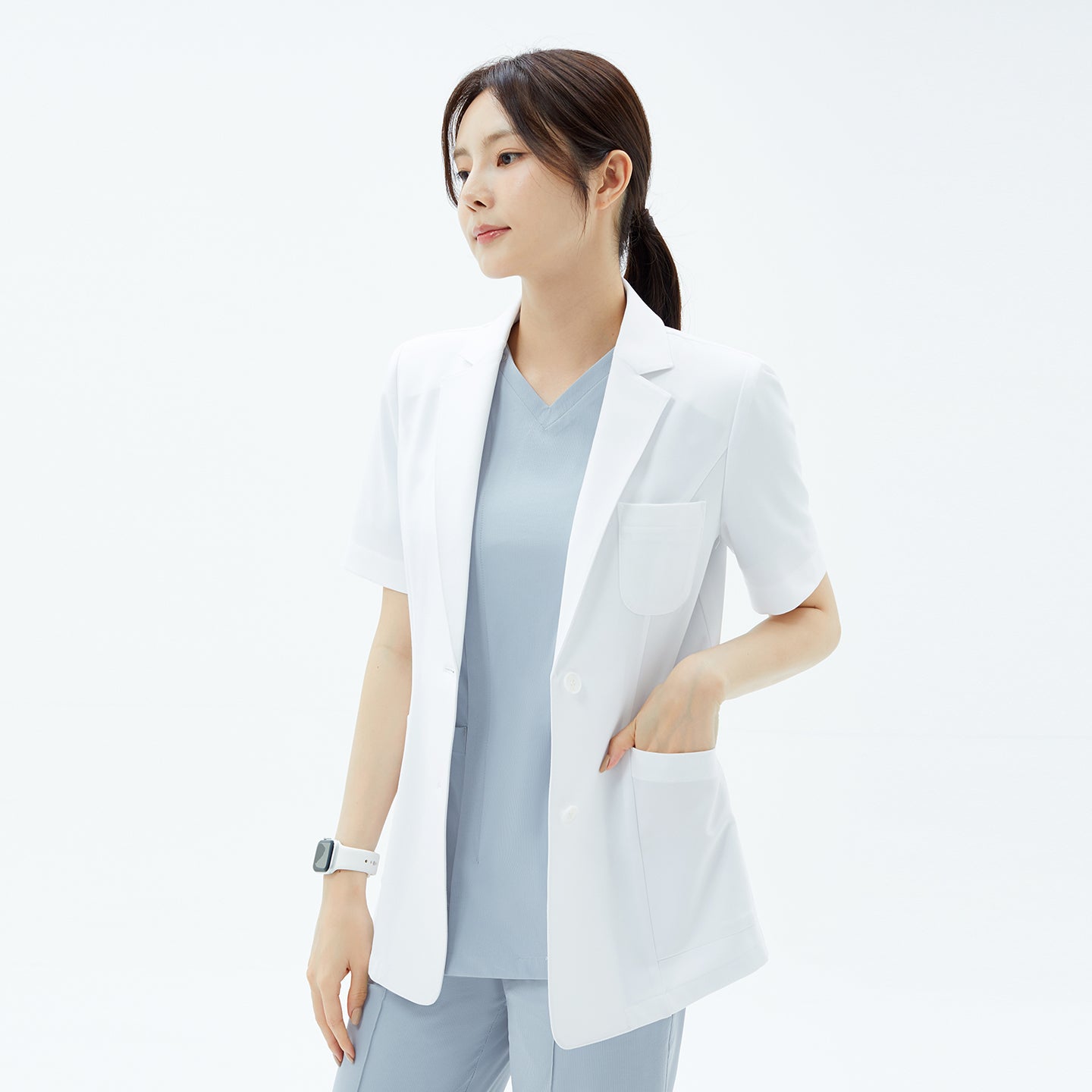 Side profile of the TUL Women’s LCW-15 Lightweight Short Sleeve Lab Coat – White, with the model’s hand in a pocket to illustrate the straight hem.