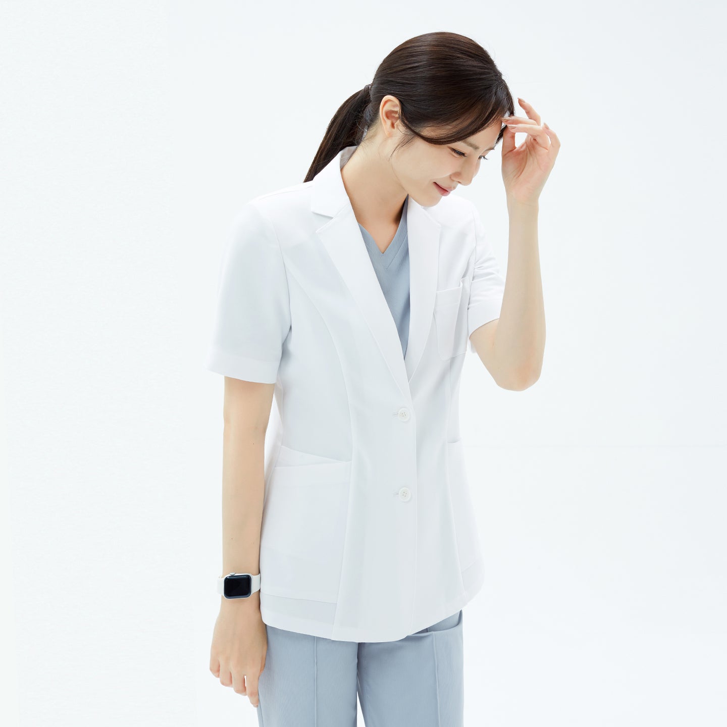 Image of Close-up of the lapel collar and chest pocket as the model adjusts her hair in the TUL Women’s LCW-15 Lightweight Short Sleeve Lab Coat – White.