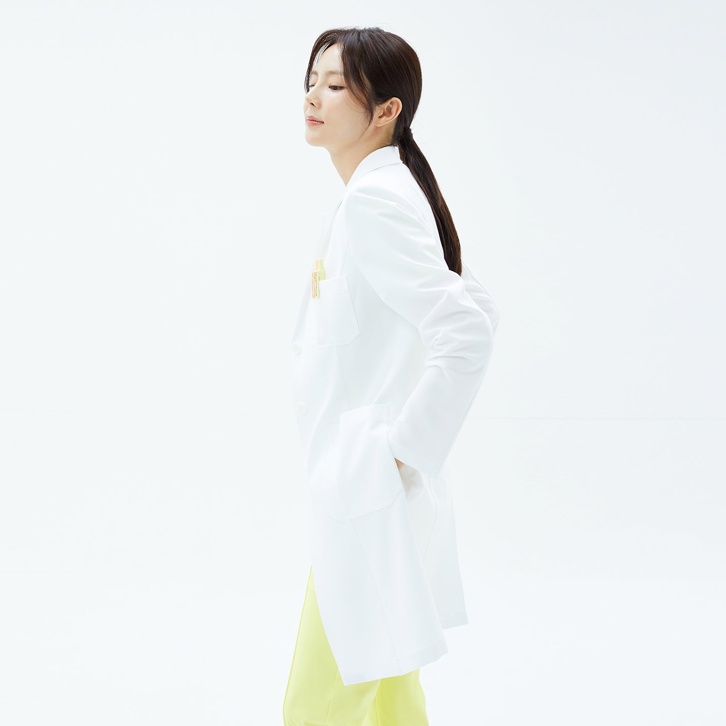 Image of Side profile of the TUL LCW-17 Straight Long Lab Coat in White with hands in pockets.