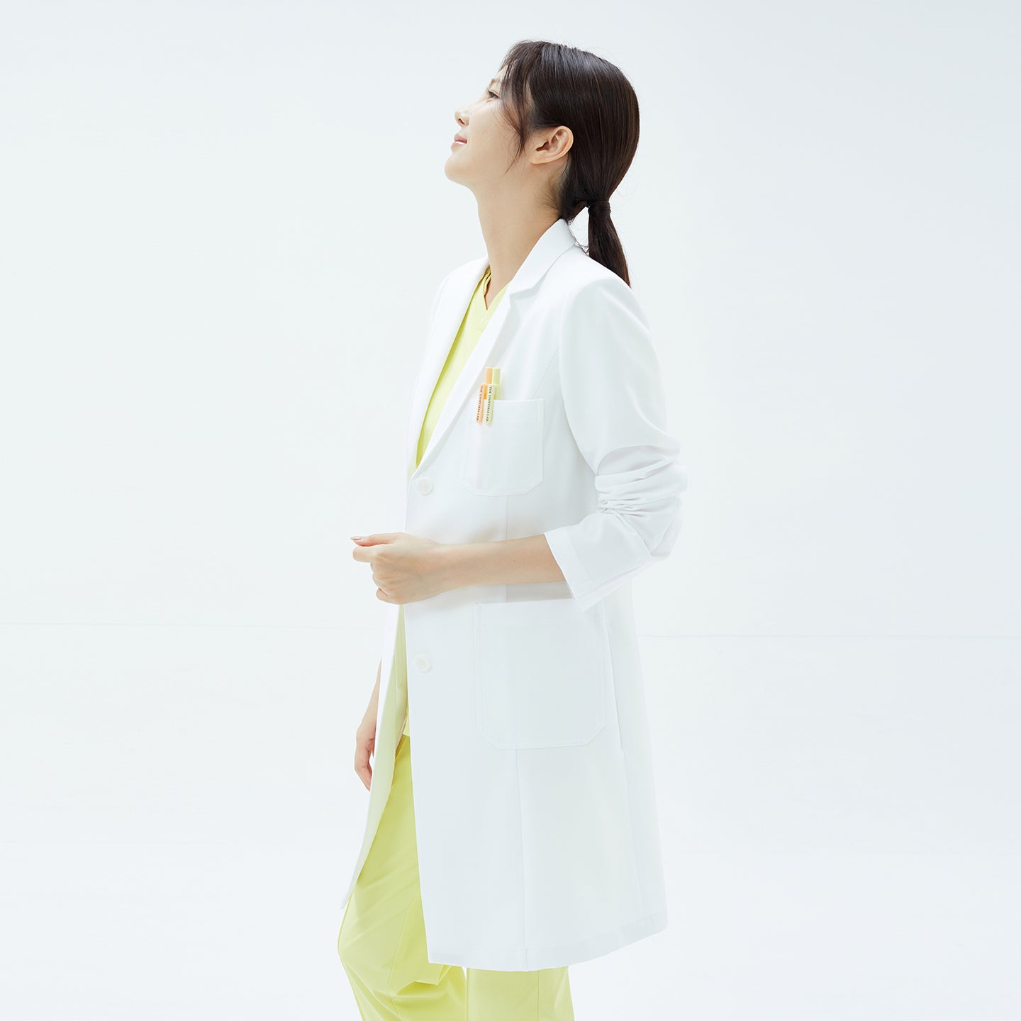 Image of Three-quarter view of the TUL LCW-17 Straight Long Lab Coat in White, sleeves lightly rolled, and model looking up.