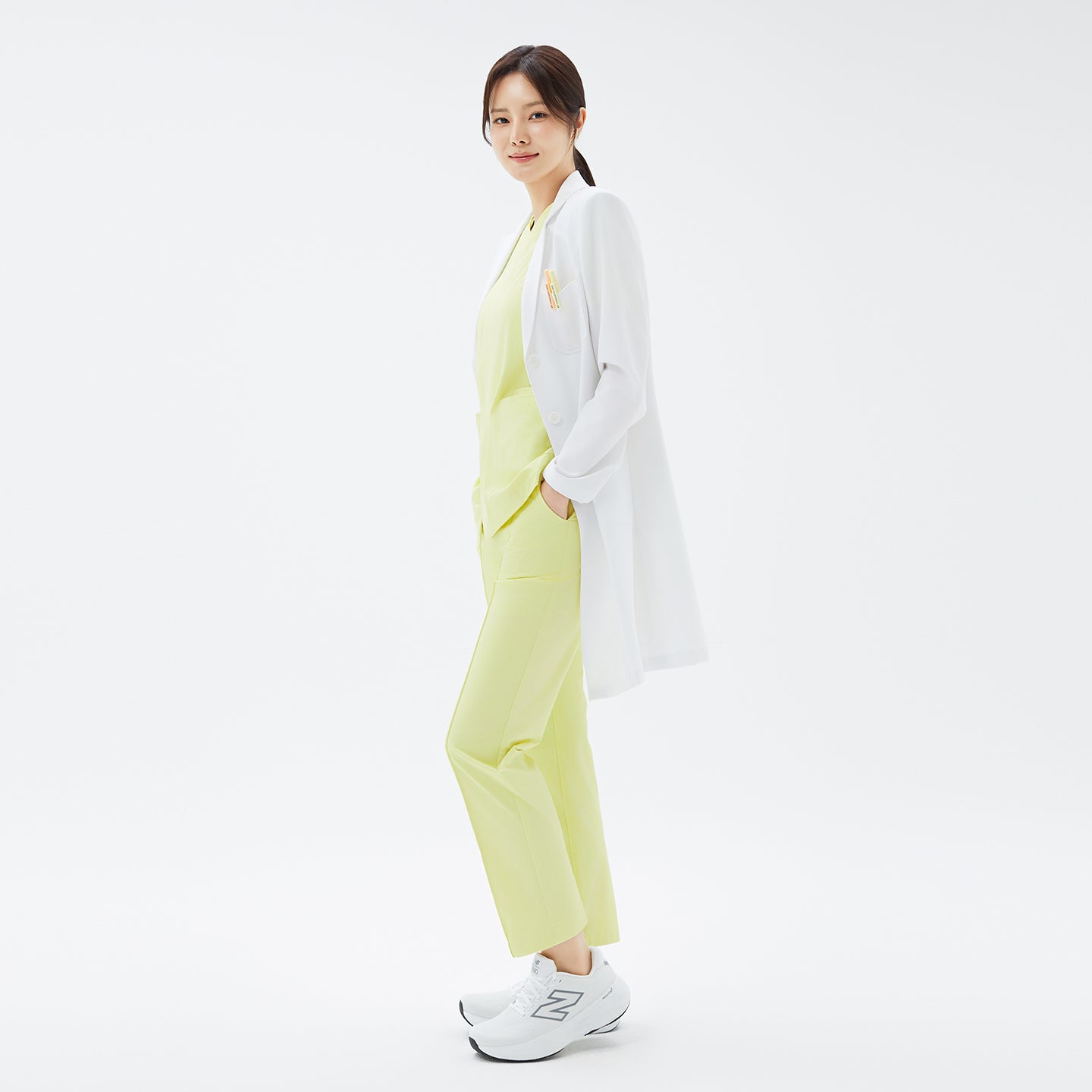 Image of Relaxed side pose in the TUL LCW-17 Straight Long Lab Coat in White paired with matching pastel scrubs.