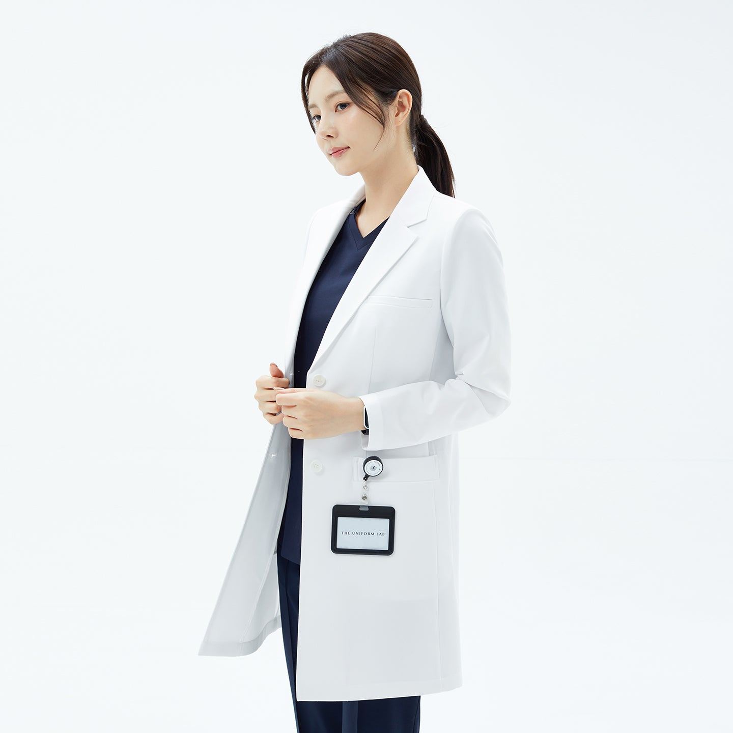 Image of Woman looking to the side in the TUL Women's LCW-18 Classic Long Lab Coat in White layered over navy uniform.